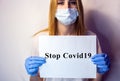 A girl in a mask on her face holds a no Covid19 sign in her hands. The tablet in the hands of a girl on a white background. Blonde Royalty Free Stock Photo