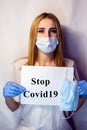 A girl in a mask on her face holds a no Covid19 sign in her hands. The tablet in the hands of a girl on a white background. Blonde Royalty Free Stock Photo