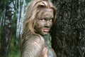 Girl with a mask of mud near a tree trunk in an ecological resort. Beautiful blonde