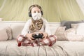 Girl in a mask playing on a game console during quarantine on the bed