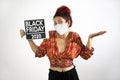 Girl with mask raising her hands and shoulders in show of resignation and conformity and holding a Black Friday 2020 poster with