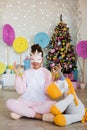 Girl in a mask with a unicorn sits near a Christmas tree