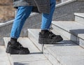 A girl in massive black boots, jeans and a checkered coat climbs up the granite stairs