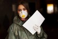 A girl medic in a mask and a protective suit is standing in the clinic with documents about the coronavirus