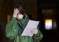 Girl medic in a mask and a protective suit stands in the clinic with documents