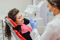 The girl in the medical chair at the dentist smiles grumbling before the treatment. A female doctor in a mask and gloves