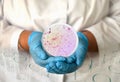 a girl in a medical gown and gloves holds a photo gonorrhea from a microscope in a round frame