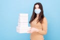 Girl in a medical mask on a blue background with lots of gift boxes. safe delivery. online shopping. space for text Royalty Free Stock Photo