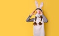 A girl with a medical mask and Easter bunny ears is holding colorful Easter eggs on a yellow background. Easter, coronavirus, Royalty Free Stock Photo