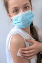 Girl in a medical mask holds cotton wool on her hand after the injection. Royalty Free Stock Photo