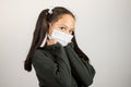 Girl with medical mask looking at the camera worried while resting her head on her hands. On white background