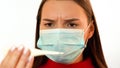 A girl in a medical mask looks at a thermometer and frowns