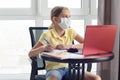 A girl in a medical mask on quarantine in isolation isolates herself remotely from her lessons and distracted, looked out the