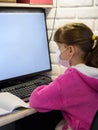 A girl in a medical mask sits at a computer and learns online Royalty Free Stock Photo