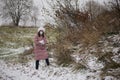 A girl in a medical mask and winter clothes on a walk in the park. Holds a ball of snow in his hand. The ground is covered with th