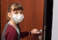 A girl in a medical protective mask opens the door from the apartment