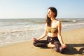 Girl meditating in lotus yoga on coast of sea on the beach. Young beautiful healthy woman making meditation on the beach