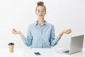 Girl meditating at work sitting in lotus pose with nirvana orbs near laptop and smartphone trying relax and get rid of