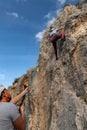 Girl in the middle of a rock wall that is climbing while her boyfriend belays her from below