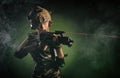 The girl in military airsoft clothes poses with a gun in her hands on a dark background