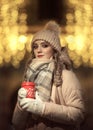 A girl in mittens and a hat holds a red coffee mug