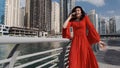 A girl of mixed race in a bright red dress walks along the Dubai Marina and admiringly talking on the phone, United Arab