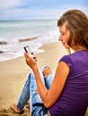 Girl with mobile phone sitting on sand near sea.