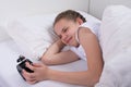 girl in the morning in bed, shows emotions, looking at the alarm clock Royalty Free Stock Photo