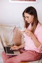 A girl in the morning in pajamas at home working on a laptop with drinking coffee, a girl self-isolated at home and resting on the