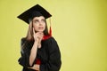 Girl in mortarboard and graduate gown standing, thinking. Royalty Free Stock Photo