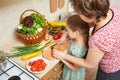 Girl and mother chopping cucumber in kitchen, vegetables and fresh fruits in basket, healthy nutrition concept Royalty Free Stock Photo