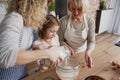 Little girl with mother and grandmother sifting flour