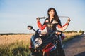 Girl in a motorcycle leather protective suit sits on the motorcycle and holds katana