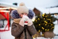 Girl with mug with snow, candy cane and inscription Merry and Bright in her hands outdoor in warm clothes in winter at festive