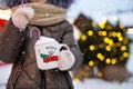 Girl with mug with snow, candy cane and inscription Merry and Bright in her hands outdoor in warm clothes in winter at festive