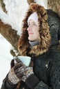 Girl with a mug of tea leaning against a tree and looking straight. Winter, outdoors Royalty Free Stock Photo