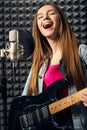 Girl musician in recording studio playing electric guitar and singing in mic Royalty Free Stock Photo