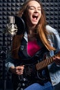 Girl musician in recording studio playing electric guitar and singing in mic Royalty Free Stock Photo