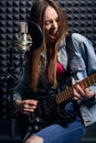 Girl musician in recording studio playing electric guitar and singing in mic Royalty Free Stock Photo