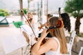 Girl musician from the string orchestra sits near the music stand and holds a cello during the wedding ceremony, back Royalty Free Stock Photo