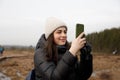 A girl in nature takes pictures on her phone. down jacket and hat Royalty Free Stock Photo