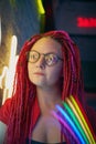 Girl in neon lights, beautiful woman in sunglasses, with pink hair, with dreadlocks pigtails, bright and stylish in glow of neon Royalty Free Stock Photo