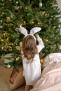 Girl in nightgown with rabbit ears on head decorates a Christmas tree in the early December morning in the bedroom Royalty Free Stock Photo