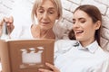 Girl is nursing elderly woman at home. They are watching photos in photo album. Royalty Free Stock Photo