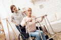 Girl is nursing elderly woman at home. Woman is trying to stand up from wheelchair. Royalty Free Stock Photo