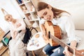 Girl is nursing elderly woman at home. Girl is playing on guitar for woman.