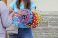 The girl offers an elderly woman to buy a wreath of artificial pink and purple flowers