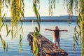 Girl on a old wooden fishing pier and willow tree enjoying beautiful sunset over the sea lake Royalty Free Stock Photo
