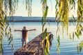 Girl on a old wooden fishing pier and willow tree enjoying beautiful sunset over the sea lake Royalty Free Stock Photo