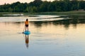 Girl paddling on SUP board on beautiful lake during sunset or sunrise, standing up paddle boarding morning adventure in Germany Royalty Free Stock Photo